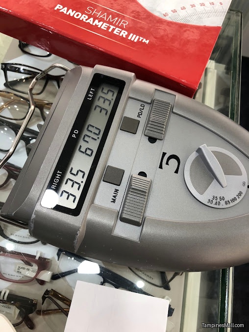 An optical device is measuring eye parameters with eyeglasses in the background.